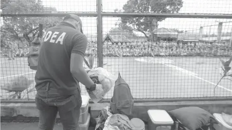  ?? KRISTINE JOYCE CAMPAÑA ?? A PDEA agent inspects personal belongings as Talisay City Jail inmates watch from a distance.