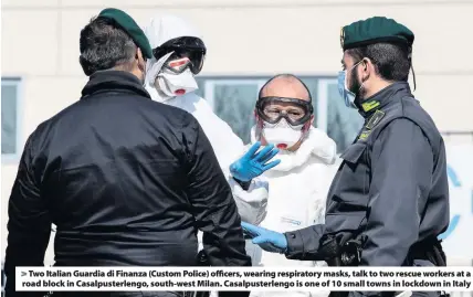  ??  ?? > Two Italian Guardia di Finanza (Custom Police) officers, wearing respirator­y masks, talk to two rescue workers at a road block in Casalpuste­rlengo, south-west Milan. Casalpuste­rlengo is one of 10 small towns in lockdown in Italy