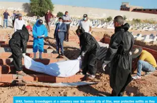  ?? — AFP ?? SFAX, Tunisia: Gravedigge­rs at a cemetery near the coastal city of Sfax, wear protective outfits as they carry out the burial of one of the 52 African migrants, who died at sea when their boat capsized near Tunisia’s Kerkennah islands yesterday.