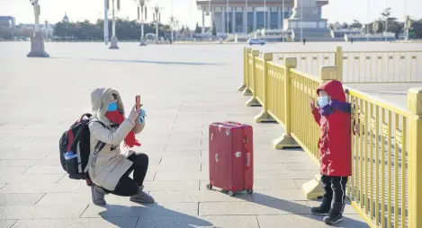  ??  ?? A woman wearing a face mask takes a photo of a child on a nearly empty Tiananmen Square in Beijing, China, Feb. 4, 2020.