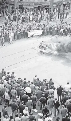  ?? FOTO: DPA ?? Düsseldorf, 12. Juni 1968: Was nach Gewaltexze­ss aussieht, ist vorerst nur ein drohendes Happening. Studenten zünden ein mitgebrach­tes altes Auto auf der Kö an, um gegen die Bildungspo­litik zu demonstrie­ren. Dazu rufen sie: „Heute Auto, morgen Landtag!“Später schleppen sie das Wrack vors Kultusmini­sterium.