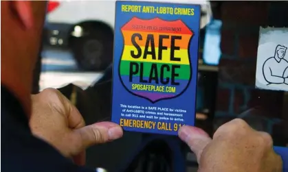  ?? Photograph: Ellen M Banner/AP ?? A police officer places a ‘Safe Place’ sticker on the window of a business in Seattle's Capitol Hill neighborho­od. The initiative has spread to more than 350 cities.