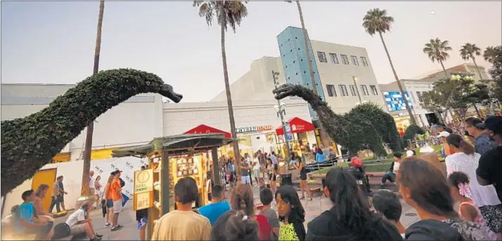  ?? Patrick T. Fallon For The Times ?? THIRD STREET PROMENADE, popular with tourists, has an abundance of street artists. Above, the crowd enjoys a performanc­e near the dinosaur topiaries.