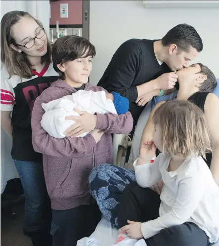  ?? BRITTON LEDINGHAM ?? Jake Muir, 10, holds his newborn brother and Calgary’s New Year’s baby, Remington James, who was born 12 seconds past midnight New Year’s Day at the Rockyview General Hospital, while father and mother Tyler and Amy kiss and sisters Teagan, 13, and Mae, 3, watch on Monday.