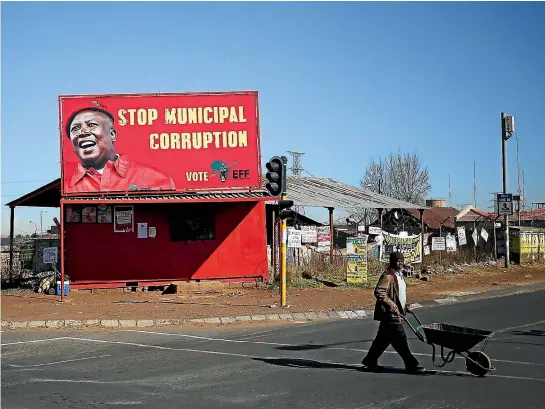  ?? REUTERS ?? A man pushes a wheelbarro­w past a billboard for the Economic Freedom Fighters (EFF) party in Soweto yesterday. South Africa’s municipal elections could see the far-Left EFF, led by President Jacob Zuma’s former protege Julius Malema, becoming kingmaker in some areas after support for the ANC collapsed.