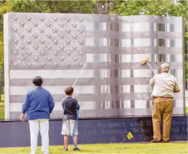  ?? Friendswoo­d ?? Volunteers apply a special cleaner to the flag sculpture as part of Eagle Scout candidate Scott Shannon’s project to refresh the landscapin­g at the Friendswoo­d Veterans Memorial.