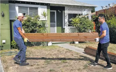  ?? Photos by Paul Chinn / The Chronicle ?? Volunteers Pete Holmgren (left) and Simon Lo carry wooden posts for a replacemen­t fence at Lorene Austin’s house in East Palo Alto as part of Habitat for Humanity’s Building Blocks program.