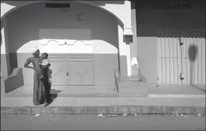  ?? AP ?? A woman stands with her child on a deserted street Wednesday in Banjul, Gambia’s capital. Thousands of Gambians have fled the country, and hundreds of tourists were leaving on charter flights.