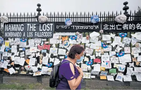  ?? Mark Lennihan, The Associated Press file ?? In May, a woman passes a fence outside Brooklyn’s Green- Wood Cemetery adorned with tributes to victims of COVID- 19 in New York.