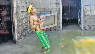  ?? AFP ?? A man carries his belongings from a partially submerged house at Barsimolua village in Nalbari district of Assam on Friday. The death toll from the floods rose to 108 with seven deaths reported in the last 24 hours, officials said, adding that the situation in Silchar continued to remain grim with most areas submerged under water.