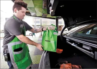  ?? AP/ ELAINE THOMPSON ?? An Amazon worker loads a bag of groceries in a customer’s car at an AmazonFres­h Pickup location in Seattle on Tuesday. The new grocery pickup service is being tested by Amazon employees and will eventually expand to serve Amazon’s Prime members. It is part of a company initiative to expand business in the food and packaged goods market.