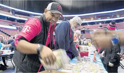  ?? TAIMY ALVAREZ/SUN SENTINEL ?? T-Mobile volunteer David LaMotta, left, packs packages of food with more than 500 other local volunteers from more than 30 Broward based companies and organizati­ons, preparing more than 300,000 meals for Broward County residents in need Tuesday at the BB&amp;T Center in Sunrise. Volunteers worked in teams to package meals that will be delivered to 25 local food banks through United Way of Broward County’s Project Lifeline program.