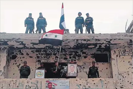  ?? SANIA THE ASSOCIATED PRESS ?? In this photo released by the Syrian official news agency SANA, Syrian military and police forces fly their national flags on a damaged building and hold a picture of Syrian President Bashar Assad, in the Hajar al-Aswad neighbourh­ood, southern...