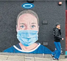  ?? /AFP (More reports inside) ?? Healing angels: A pedestrian walks past street-art graffiti, by the artist @akse_p19, depicting a nurse in scrubs and a face mask, but with an angel’s halo above her head, in Manchester, northern England, on Wednesday. The number of suspected and confirmed deaths from coronaviru­s in Britain has risen to 48,000, official data showed on Tuesday.