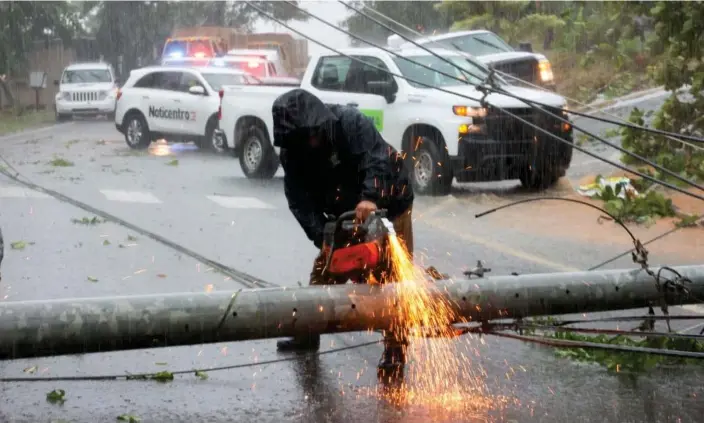  ?? Photograph: Stephanie Rojas/AP ?? A worker cuts an electricit­y pole that was downed by Hurricane Fiona as it blocks a road in Cayey, Puerto Rico, on Sunday.