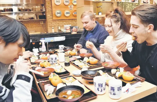  ?? — The Japan News photo ?? Foreign tourists taste a new sushi menu in Fukuyama, Hiroshima Prefecture.