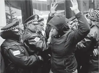  ?? JOSHUA LOTT, GETTY IMAGES ?? Police officers watch a demonstrat­or put her hands up as she blocks the entrance to the Under Armour store Friday on Michigan Avenue to protest the shooting of Laquan McDonald.