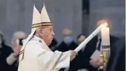  ?? REMO CASILLI/REUTERS ?? Pope Francis lights a candle Saturday at an Easter vigil service in a nearly empty St. Peter’s Basilica.