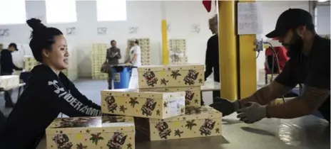  ?? MELISSA RENWICK/TORONTO STAR ?? Diana Wong, a Santa Claus Fund volunteer from Under Armour, pushes gift packages towards Caitlan Belasco at the Toronto Star warehouse.