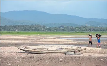  ?? PATIPAT JANTHONG ?? Villagers walk past an abandoned boat in Chon Buri’s dried-up Bang Phra reservoir. El Nino is expected to cause continued drought and lower farm production in Thailand next year.