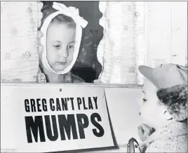  ?? CP PHOTO ?? In a 1957 photo Jon Douglas, 6, visits his friend, Greg Cox, standing behind a sign warning he has mumps, on the door of his home in Altamont, Ill.