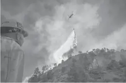  ?? TRIBUNE NEWSSERVIC­E ?? Los Angeles County firefighte­r Tommy Davis watches a water-dropping helicopter make a drop on the Bobcat Fire last month.