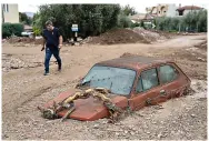  ?? The Associated Press ?? ■ A man walks next to a damaged car Thursday after floods in the town of Agria near the city of Volos, Greece. A second powerful storm in less than a month hammered parts of central Greece, sweeping away roads, smashing bridges and flooding thousands of homes.