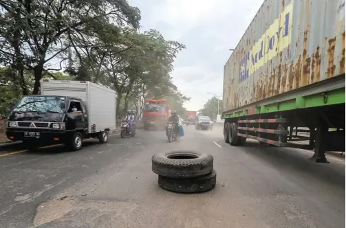  ?? ALLEX QOMARULLA/JAWA POS ?? BIAR TAK PICU CELAKA: Warga menutup lubang di Jalan Margomulyo dengan ban agar tak ada pengendara motor yang terperosok.