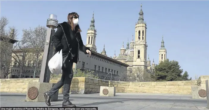  ?? ÁNGEL DE CASTRO ?? Una mujer atraviesa el Puente de Piedra de Zaragoza, ayer, protegida con una mascarilla.