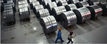  ?? — AFP ?? Output falls: A file picture shows workers walking in a warehouse in the Han-steel plant in China. Chinese steel output fell to 71.83 million tonnes in September from 74.59 million tonnes the month before.