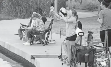  ??  ?? A girl checks her line as people fish at Veterans Oasis Park in Chandler.