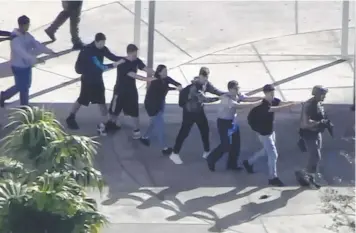  ?? Pictures: AP ?? EVACUATION: Students, their hands in plain sight, are led from the school by a SWAT gunman; and (right) distraught parents comfort one another as they wait for news of loved ones.