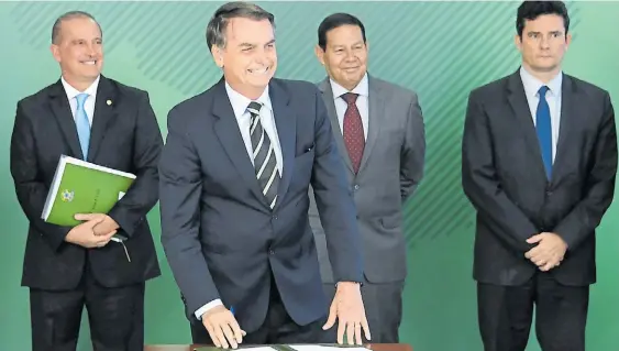  ?? AFP ?? Gesto. El ex capitán del ejército Jair Bolsonaro, con algunos ministros, al firmar ayer el decreto que facilita la venta de armas de fuego en Brasil.