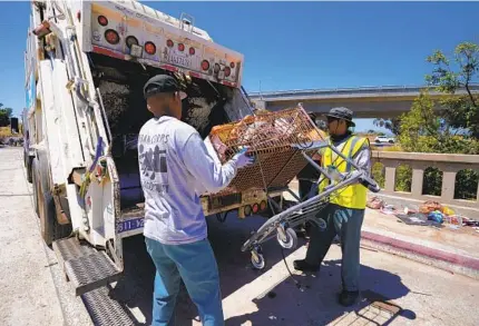  ?? NELVIN C. CEPEDA U-T ?? A San Diego city crew throws a shopping cart collected from an Anna Avenue homeless camp into a trash truck in June.