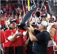  ?? STEVE MARCUS — THE ASSOCIATED PRESS ?? Utah coach Kyle Whittingha­m, right, hands the trophy to QB Cameron Rising, center, after Utah defeated Southern California in the Pac-12 Conference championsh­ip.