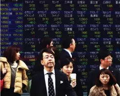  ??  ?? TOKYO: Pedestrian­s pass before a share prices board in Tokyo. Tokyo stocks dropped on a stronger yen, with Toshiba slumping on a weekend report that the scandal-hit conglomera­te will likely post a massive fiscal year loss.— AFP