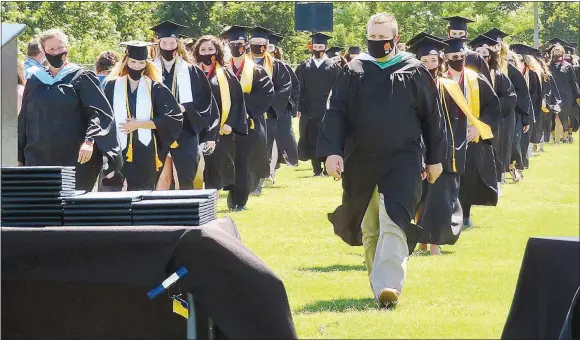  ?? Westside Eagle Observer/RANDY MOLL ?? Led by assistant principal Taos Jones, masked graduates of Gravette High School march into Lion Stadium on Sunday afternoon before being seated with parents and guardians on the field.