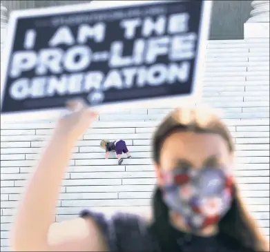  ??  ?? THE OPPOSITION: As a tot frolics on the Supreme Court steps Monday, an anti-abortion activist demonstrat­es.