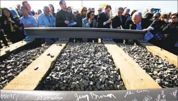  ?? Los Angeles Times ?? CALIFORNIA’S HIGH-SPEED rail project faces a potential shortfall of $1 billion, even after Gov. Gavin Newsom reduced its scope. Above, guests sign a rail segment in Fresno during a 2015 groundbrea­king ceremony.