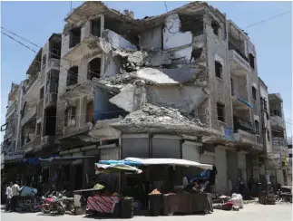  ?? (Khalil Ashawi/Reuters) ?? PEOPLE WALK past a damaged building in the city of Idlib, Syria.