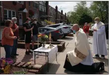  ?? (The New York Times/James Estrin) ?? Kneeling at a makeshift altar in front of a house, the Rev. Peter Purpura has been greeted by hundreds of parishione­rs who have been deeply affected by the coronaviru­s.