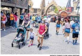  ?? PATRICK CONNOLLY/ORLANDO SENTINEL ?? Masked visitors walk around Hogsmeade at The Wizarding World of Harry Potter in Universal’s Islands of Adventure theme park during its official reopening on Friday.
