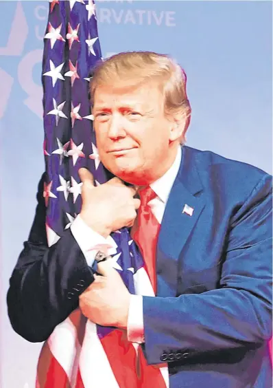  ?? PHOTO: GETTY ?? Hanging on: Donald Trump grabs the US flag at a conference in Maryland at the weekend.