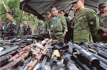  ??  ?? DUTERTE (tengah) melihat senjata api yang dirampas daripada militan ketika melawat sebuah kem tentera di Marawi kelmarin. - AFP