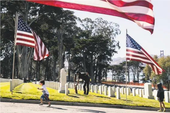  ?? Stephen Lam / Special to The Chronicle ?? Alex Molina (center) holds a guitar as he reads a gravestone in San Francisco National Cemetery with his young relatives. Few are traveling amid the pandemic.