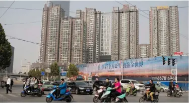  ??  ?? ZHENGZHOU: People ride electric bikes as they pass next to property condominiu­ms (back) in Zhengzhou yesterday. China’s growth slipped to a seven-year low of 6.6 percent in the third quarter, according to an AFP survey, despite ample stimulus and a...