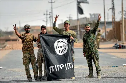  ?? REUTERS ?? Shi’ite Popular Mobilisati­on Forces show off a captured Islamic State flag after liberating the Iraqi town of al-Qaim from the jihadists.