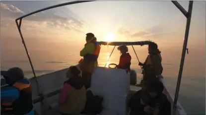  ??  ?? Chen Mo (first from left) and Yang Chengteng (second from left) look into the distance at sunset, after leaving Xieyang Island.