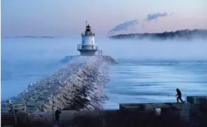  ?? (AP Photo/robert F. Bukaty) ?? A man walks of the sea wall Saturday near Spring Point Ledge Light in South Portland, Maine. The morning temperatur­e was about -10 degrees Fahrenheit.