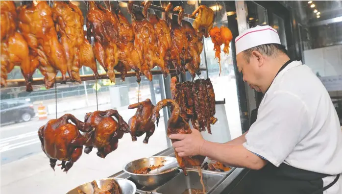  ?? VICTOR HILITSKI/FOR THE SUN-TIMES ?? Ducks, chickens, cuttlefish and barbecue pork hang in a case in the store’s window as Tang Thanh, one of the Sun Wah barbecue cooks, prepares its famous roasted duck for a customer.